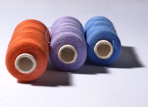 three large spools of thread, one orange, one purple, and one blue, against a white background