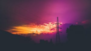a metal framework tower holding up power lines is silhouetted against a dark sky that appears to be photoshopped because it is purple